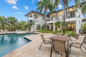 A modern two-story house with a pool, outdoor seating, and palm trees.