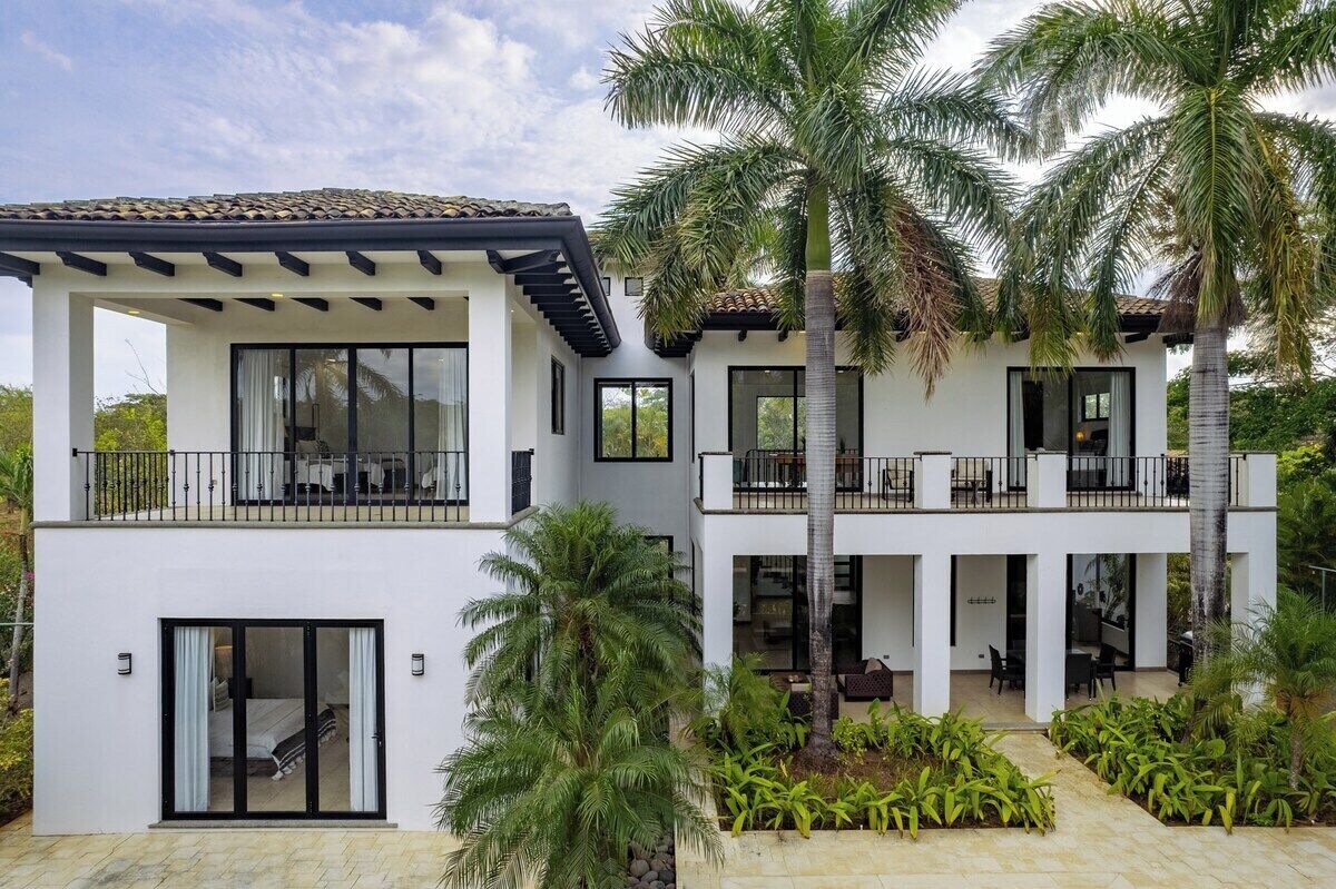 A modern two-story building with balconies, large windows, and a courtyard with palm trees.