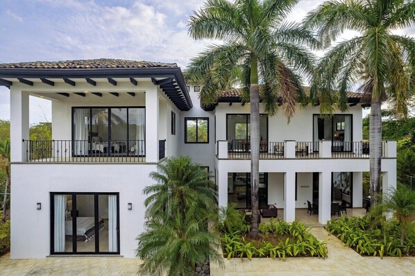 A modern two-story building with balconies, large windows, and a courtyard with palm trees.