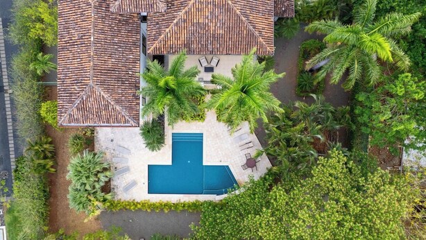 An aerial view of a property with a swimming pool, surrounded by palm trees and a tiled roof.