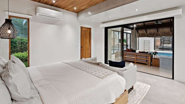 A modern bedroom with a large bed, a wooden ceiling, and a view of an outdoor swimming pool.