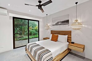 Un dormitorio moderno con una cama grande, un ventilador de techo y vistas a la vegetación a través de puertas correderas.