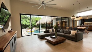 A spacious living area with a large window, a ceiling fan, and a dining area with a pool view.
