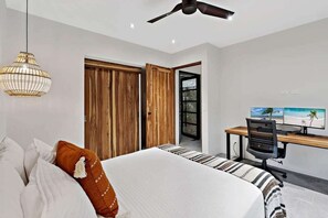 Ein Schlafzimmer mit einem Bett, einem Schreibtisch mit Computer, einem Deckenventilator und einem großen Fenster.
