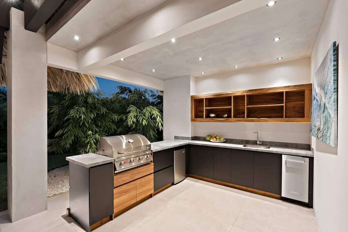 Una cocina moderna con una parrilla empotrada, muebles oscuros y vistas a zonas verdes.