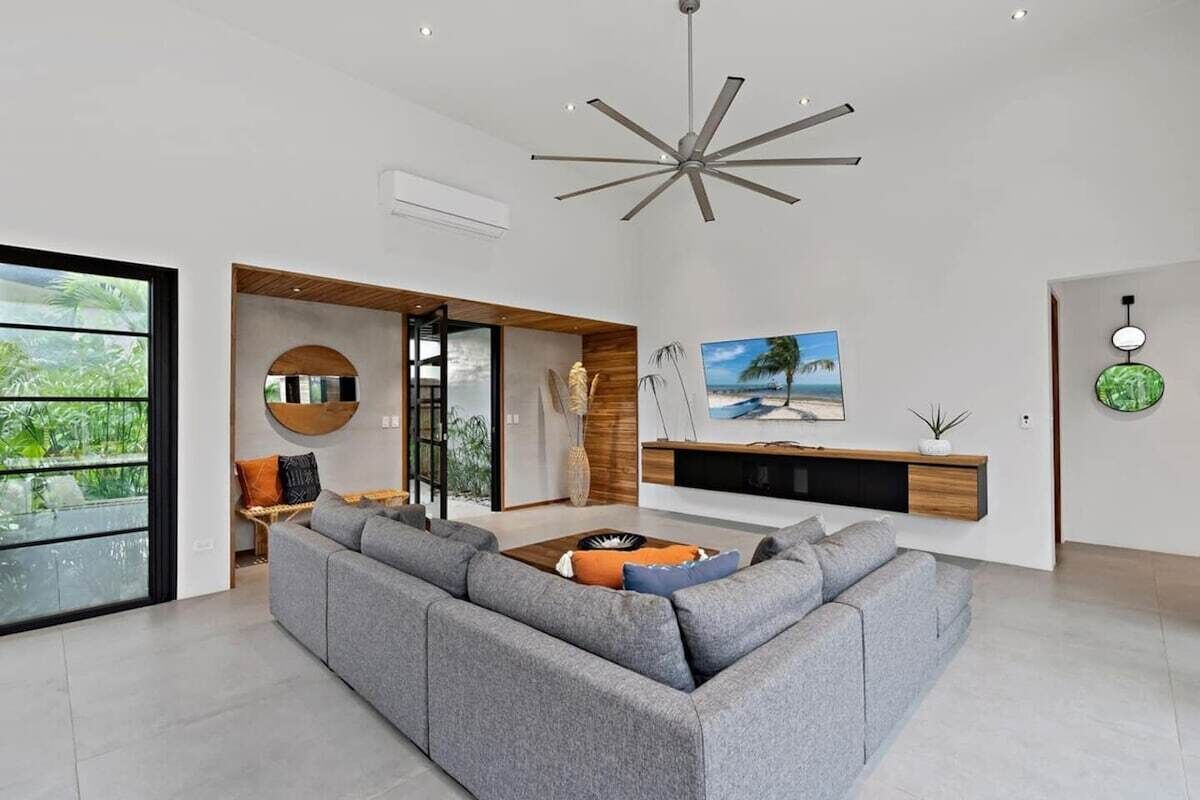 A modern living room with a sectional sofa, a ceiling fan, and a large window.
