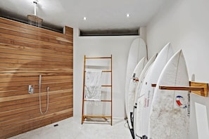 Un bany modern amb un mur de panells de fusta, una dutxa i uns quants surfboards penjats a la paret.