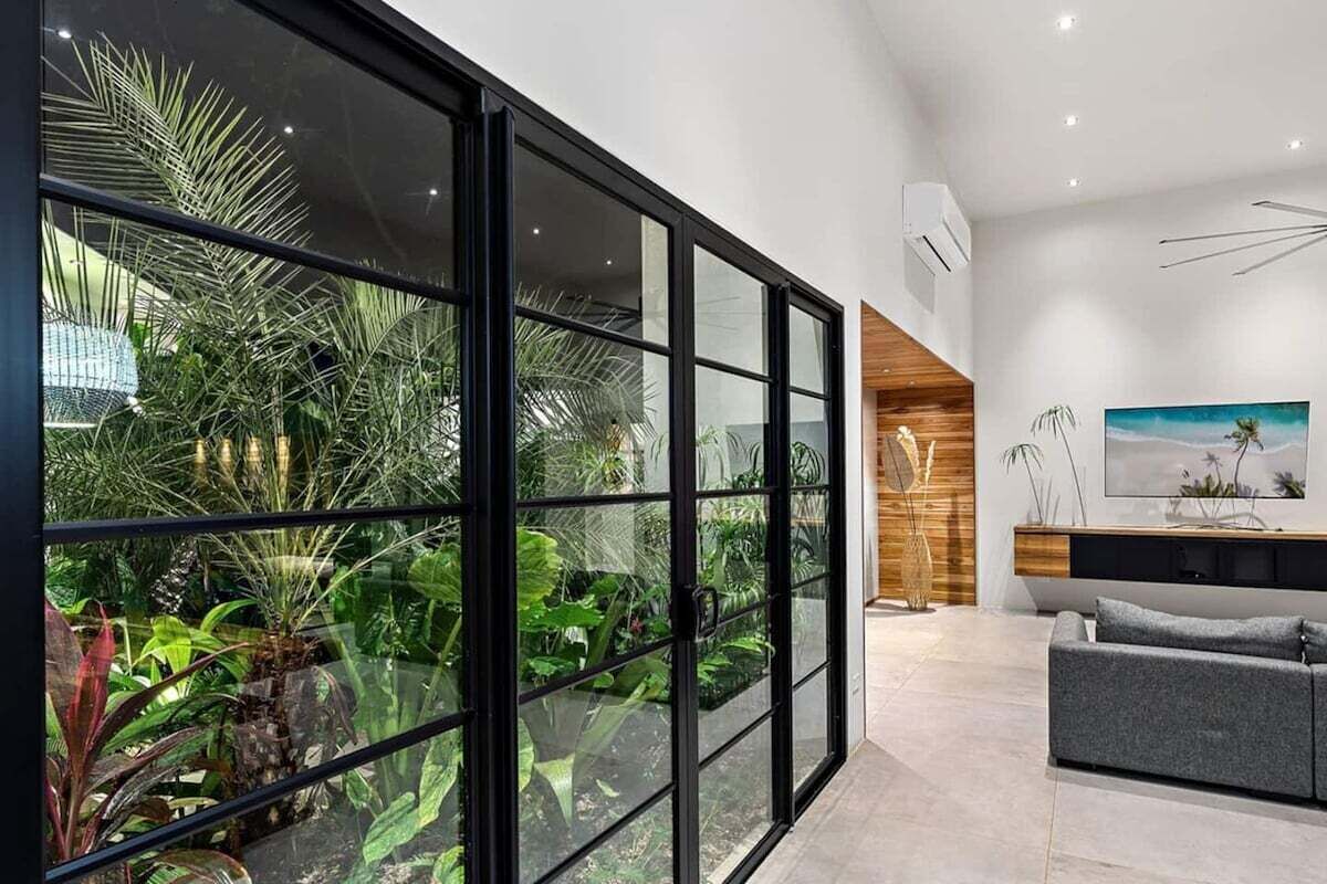 Un salón moderno con un separador de vidrio, un sofá gris y una pared de acento de madera.
