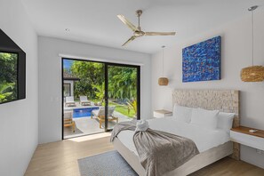 A modern bedroom with a large bed, a ceiling fan, a view of a pool, and a blue abstract painting. - Luxury property with private pool, Beach Club Access, daily housekeeping, concierge services (Reserva de Golf 84, Hacienda Pinilla)