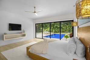 Quarto moderno com uma cama grande, televisão e vista para uma piscina.