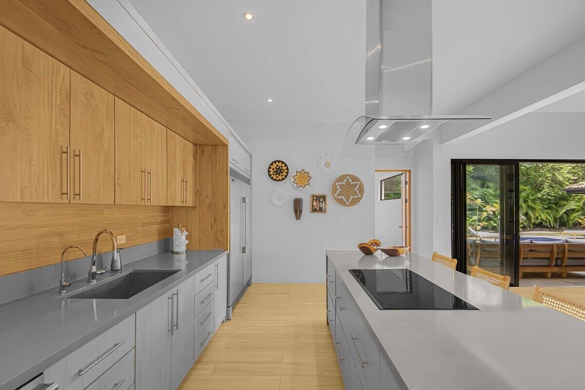A modern kitchen with wooden cabinets, a large island, and a view of the outdoors.
