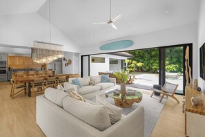 A modern interior with a dining area, a living room with a sofa and coffee table, and a view of the outdoors through large windows. - Casa Prana (Reserva de Golf 84, Hacienda Pinilla)