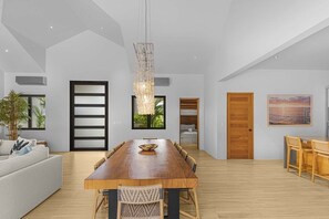 A spacious living area with a large wooden dining table, a sofa, and a hanging light fixture.