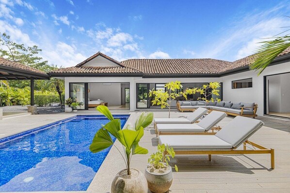 A modern house with a swimming pool, lounge chairs, and a garden.