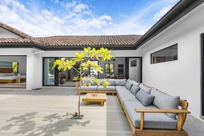 A modern house with a patio, a wooden bench, a sofa, and a tree.