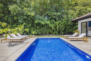 A rectangular swimming pool with a tiled deck, surrounded by lounge chairs and tropical plants. - Casa Prana (Reserva de Golf 84, Hacienda Pinilla)
