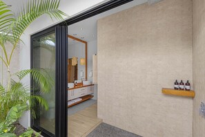 A modern bathroom with a large mirror, wooden vanity, and a shelf with toiletries. - Casa Prana (Reserva de Golf 84, Hacienda Pinilla)