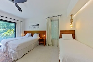 A hotel room with two beds, a ceiling fan, a nightstand, a window with curtains, and a wall-mounted light fixture.