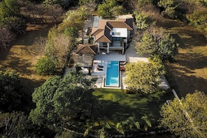 A modern house with a swimming pool, surrounded by trees and a well-maintained lawn.
