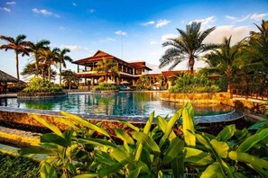 A resort with a swimming pool, palm trees, and a building with a red roof.