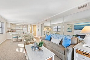 A modern living room with a sofa, coffee table, and a dining area with chairs and a table.