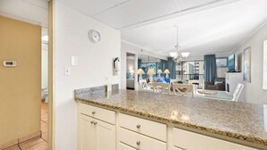 Una cocina moderna con encimeras de granito, armarios blancos y un comedor con sillas blancas.