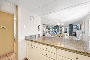 A modern kitchen with granite countertops, white cabinetry, and a dining area with white chairs.