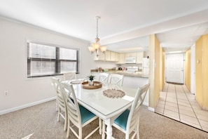 A dining area with a glass table, white chairs, and a chandelier.