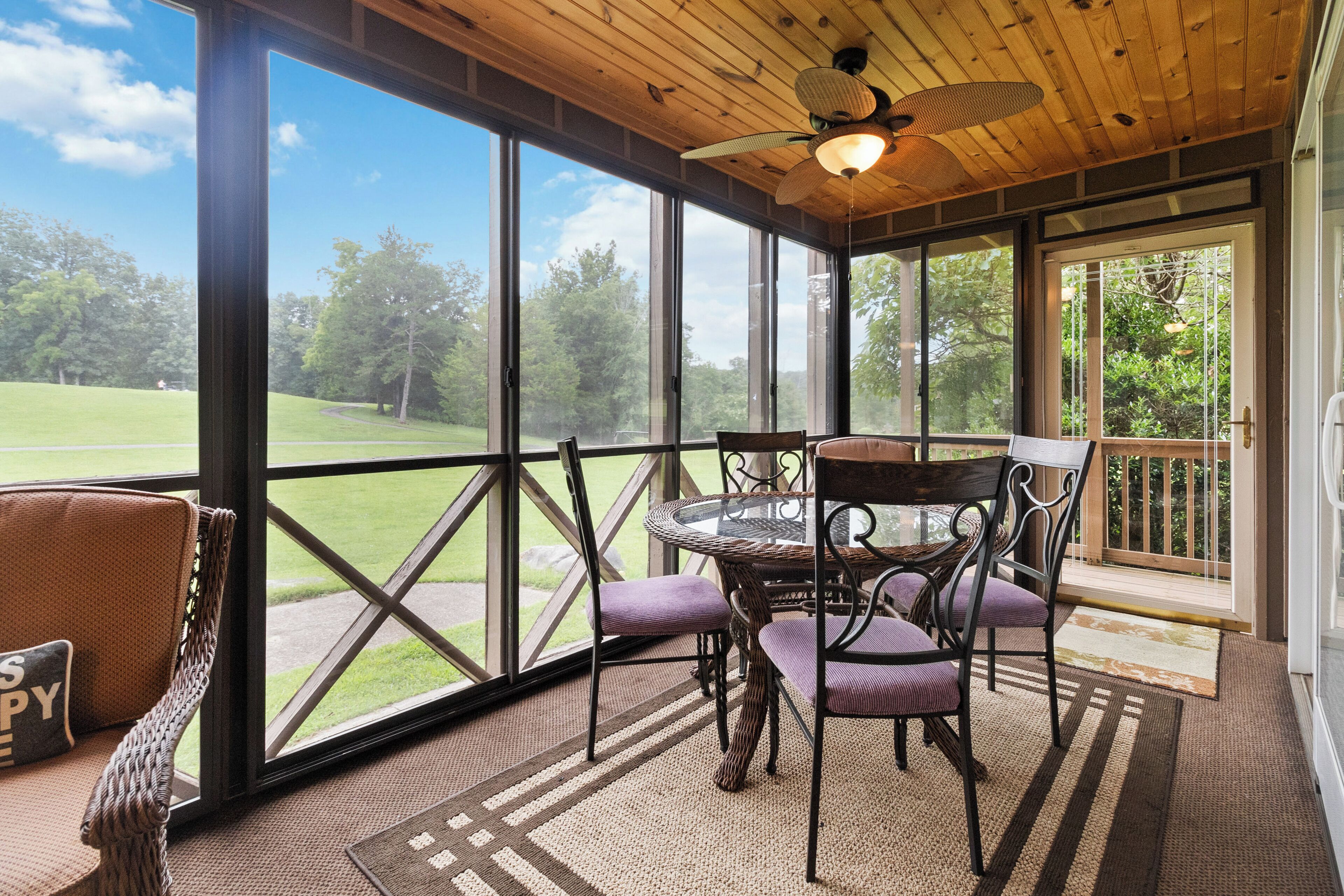 A covered patio with a table and chairs, large windows, and a view of a grassy area.