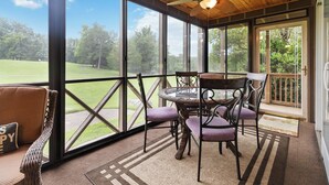 Un patio techado con una mesa y sillas, ventanas amplias y vistas a una zona con césped.