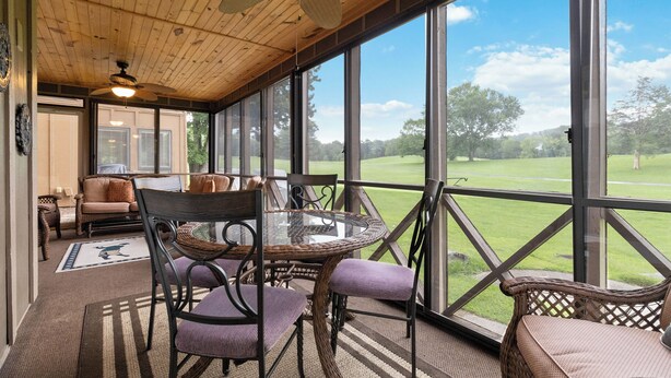 Un patio cubierto con mobiliario de mimbre, ventanas amplias y vistas a un campo de golf.