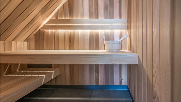A sauna with wooden walls and benches, a bench with a bucket, and a lighted shelf. - 4 bedroom gorgeous home in Den Ham (Den Ham)