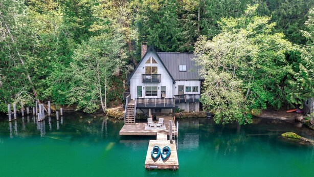 Una casa con un muelle que se adentra en un lago, rodeada de un bosque denso.
