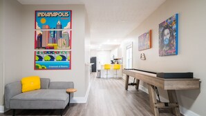 Uma sala de estar moderna com um sofá cinzento, almofadas amarelas, uma mesa de centro de madeira e uma obra de arte com tema urbano.