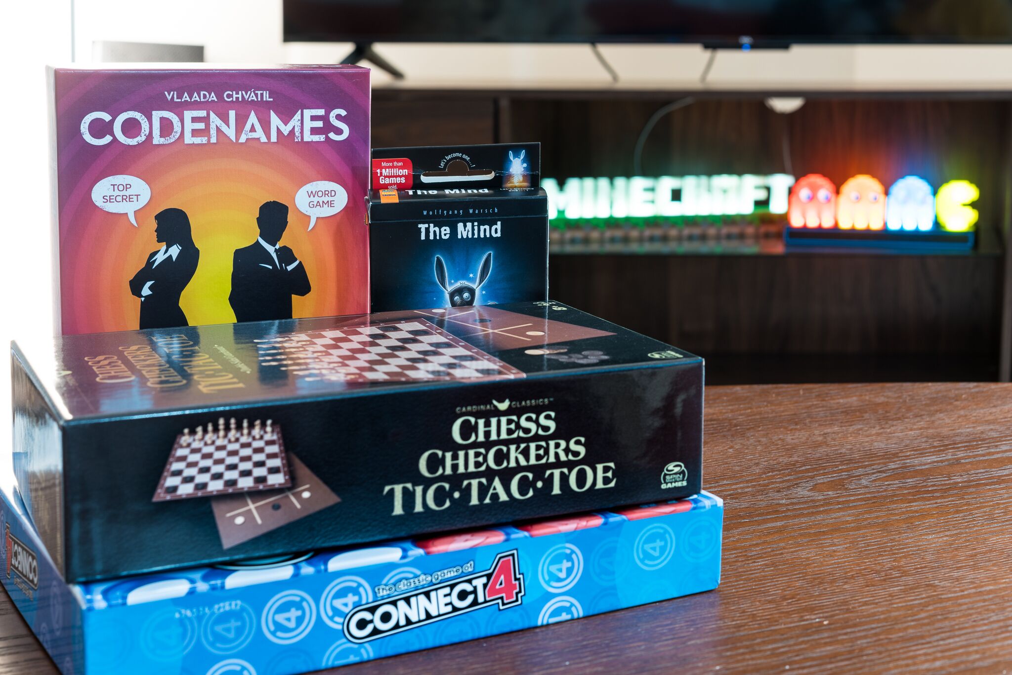 A stack of board games including Codenames, The Mind, Chess Checkers Tic-Tac-Toe, and Connect 4.