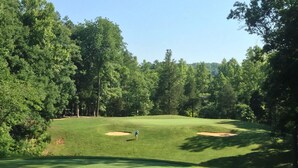 A golf course with a well-maintained green, sand bunkers, and a clear sky.