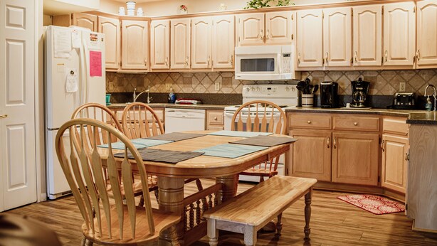 A kitchen with wooden cabinets, a microwave, a stove, and a dining table with chairs.