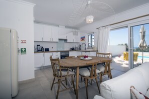 Eine moderne Küche mit weißen Schränken, einem Holztisch und Blick ins Freie.