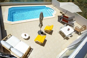 Ein Poolbereich auf dem Dach mit Whirlpool, gelben Liegestühlen, einem Tisch und einem Sonnenschirm.