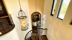 Una escalera de caracol con barandilla de madera y balaustrada de metal, que conduce a un rellano con un farol y un vitral.