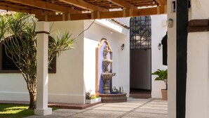 Un patio con una fuente, plantas en macetas y una pérgola.