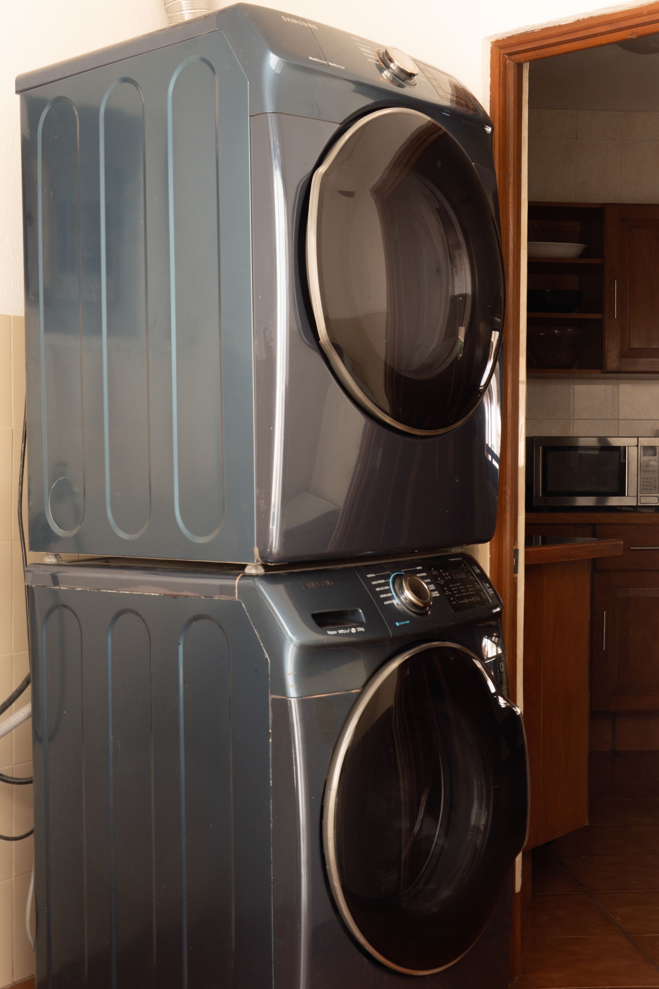 A stacked washer and dryer in a kitchen area with wooden cabinets and a microwave.