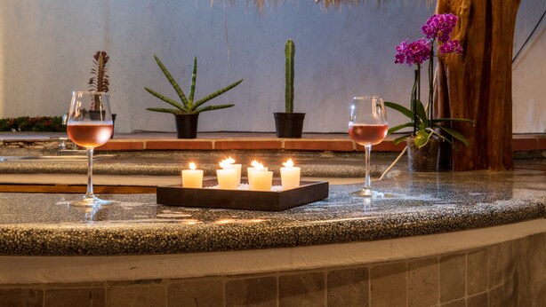 Una zona de bar con mostrador de piedra, velas y plantas en macetas.