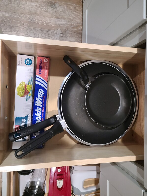 A kitchen drawer containing a frying pan, a box of aluminum foil, and a box of wrap.