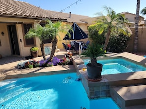 Una piscina con borde de baldosas, rodeada de plantas en macetas y un patio con mobiliario exterior.