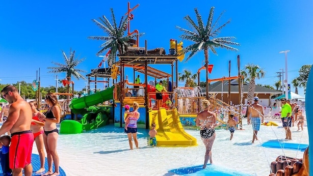 Een waterpark met glijbanen en zwembaden, palmbomen en mensen die van de voorzieningen genieten.