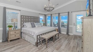 Een slaapkamer met een groot bed, een bankje, een nachtkastje en een kroonluchter.