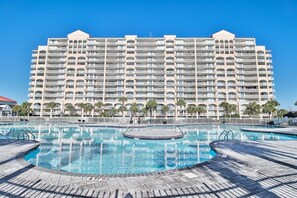 Un grand hôtel doté de nombreux balcons, d’une piscine centrale et d’un jacuzzi circulaire, le tout sous un ciel d’un bleu éclatant.