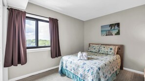 A bedroom with a bed, a window with curtains, a painting on the wall, and a view of the outdoors.