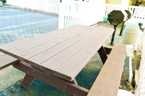Una mesa de picnic de madera con bancos, una piscina al fondo y una cerca blanca.